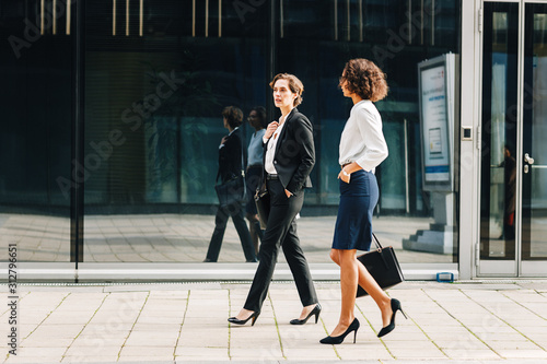 Two women commuting to the office in the day carrying office bags. Ceo and her assistant walking on a city street.