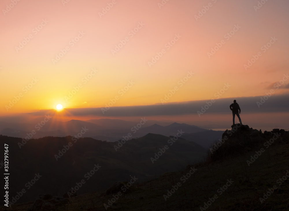 Mountaineer on a rock with the sun at sunset, Gipuzkoa from Mount Jaizkibel, Euskadi