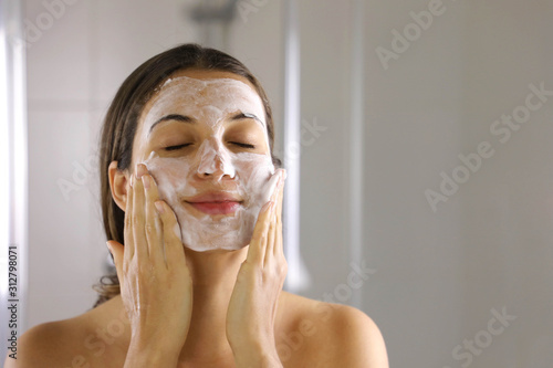 Skincare woman washing face  foaming facewash soap scrub on skin. Face wash exfoliation scrub soap woman washing scrubbing with skincare cleansing product. Enjoying relaxing time.