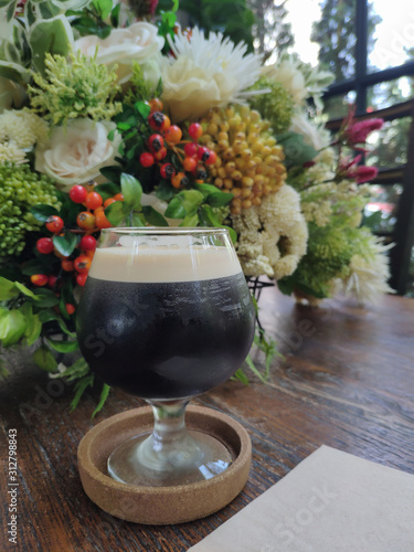 Nitro cold brew coffee, is cold brew coffee charged with nitrogen to give it a rich, creamy head on the wooden table and flower background