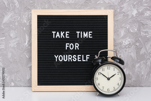 Take time for yourself. Motivational quote on letterboard and black alarm clock on table against stone wall. Concept inspirational quote of the day photo