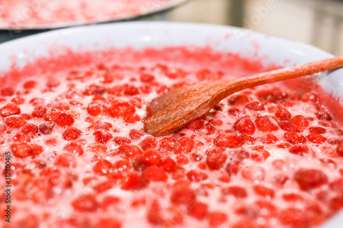 Strawberry jam cooking process. Wooden spoon liying on jam surface. Organic traditional jam manufacturing. photo