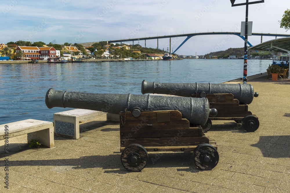 Close up view of old medieval artillery canons on nature landscape background. Beautiful Queen Juliana Bridge across St. Anna Bay in Willemstad. 