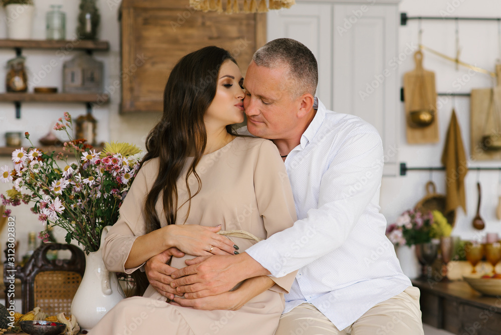 First pregnancy. Concept-a happy man hugs his pregnant wife's stomach while sitting in the kitchen. The wife kisses the future father. First pregnancy. Concept-a happy man hugs his pregnant wife's stomach while sitting in the kitchen. The wife kisses the future father.