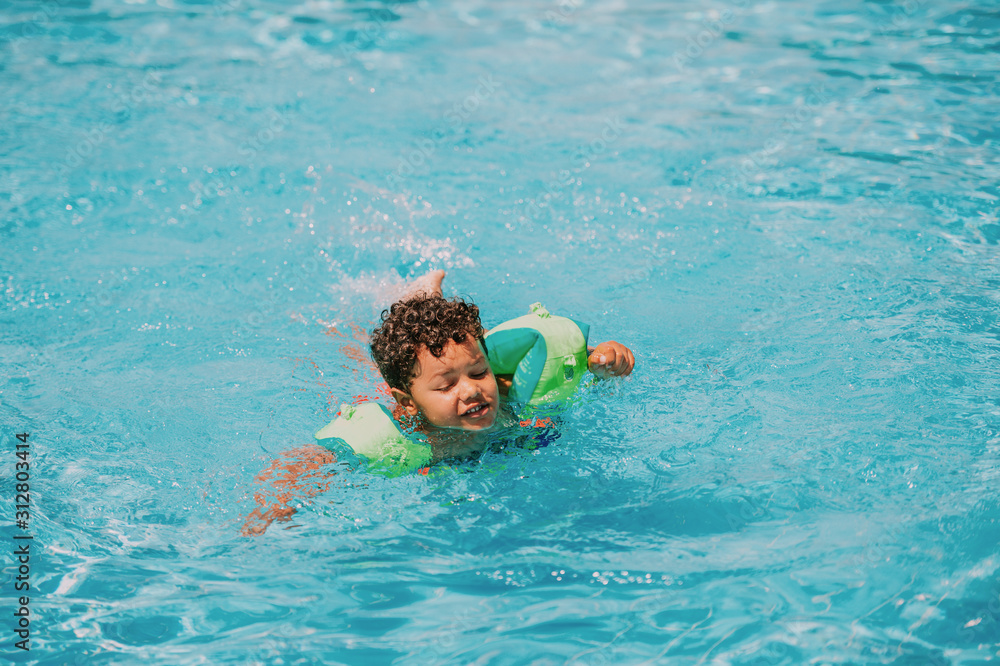 Cute african toddler boy swimming in pool with inflatable arm rings