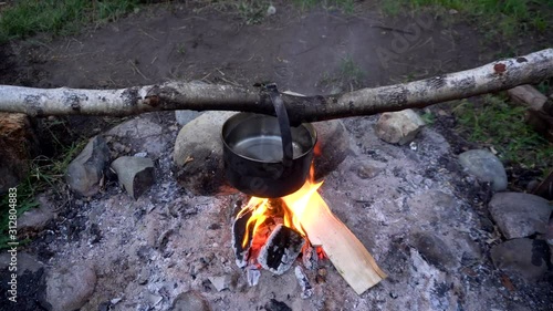 Cooking at the campfire in the woods on a hike. A pot of water for tea or soup hanging over an open fire. 4k footage.