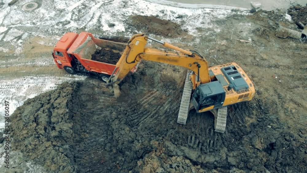 Aerial view from above of a construction site with excavators and trucks working. A loader puts stones and sand into a truck. Aerial view from above of a construction site with excavators and trucks working. A loader puts stones and sand into a truck.