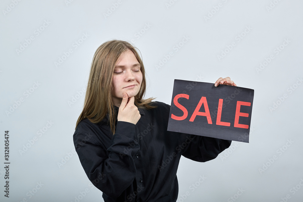 Attractive blonde woman, keeping adverising sale, keeping hand on chin, thinking wearing black shirt isolated on gray background in studio. People sincere emotions, lifestyle concept. Attractive blonde woman, keeping adverising sale, keeping hand on chin, thinking wearing black shirt isolated on gray background in studio. People sincere emotions, lifestyle concept.