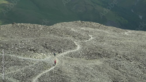 Aerial view a couple of tourists walk on a high mountain stone path. The concept of running through rough terrain. Trail running. 4k footage.
