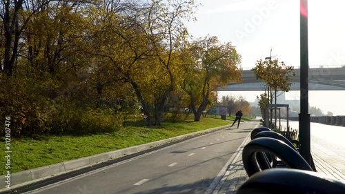 A sports young man at a morning training session on roller skates in a public city park. Sun glare and rays in the frame. The view from behind. 4k footage.
