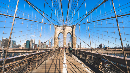 Unidentified people walk and ride bicycle on Brooklyn bridge in New York City, sunny day. United states tourism landmark, American city life, USA tourist attraction, or commuter transportation concept © Urbanscape