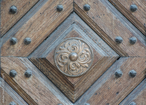 Old shabby bronze circle with a beautiful ornament on a wooden door