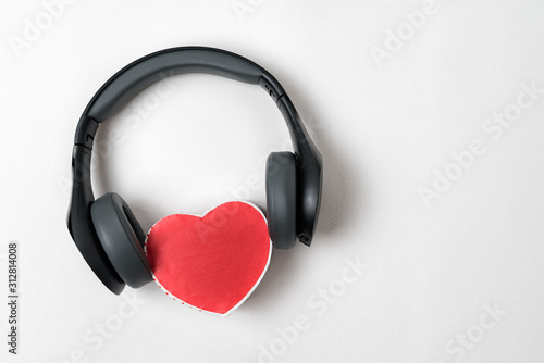 Full-size wireless headphones pulled over small red heart-shaped box on white table. Love music concept. Directly above