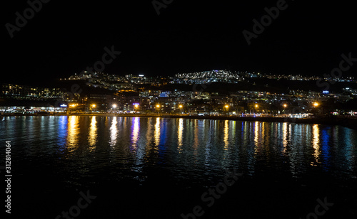 Night photography of the city with blue and yellow lights reflecting in the ocean. Puerto Rico, Gran Canaria, Spain.