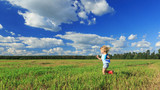 Little girl holding a paper plane in a hand and running in a field.
