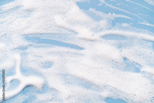 Foto White soapy foam on a blue background. Cleaning/Washing concept..