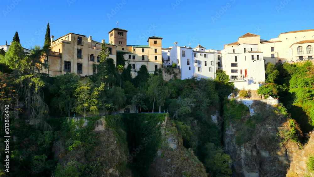 viele Häuser reihen sich am Felsrand von Ronda entland des steilen Abhangs  unter blauem Himmel