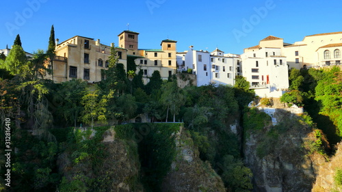  viele Häuser reihen sich am Felsrand von Ronda entland des steilen Abhangs unter blauem Himmel