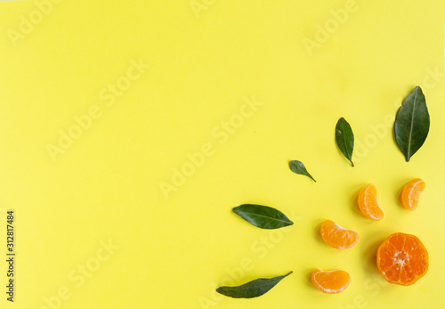 Flat lay with orange tangerines, mandarin slices, leaves on yellow background.  Top view, copy space.  