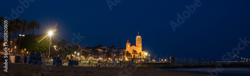 Early morning view of the beach coast in Sitges town near Barcelona in Catalonia,Spain with illuminated Parroquia de Sant Bartomeu i Santa Tecla church.