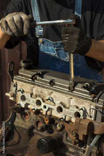 Mechanik samochodowy w stroju roboczym odkręca śruby w silniku. Odkręcanie pokrywy zaworów silnika samochodowego.