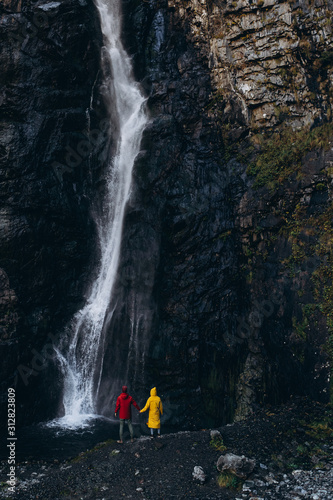 noise effect, selective focus: miniature tourist dressed in a bright colored raincoat that is contrastingly visible on a large scale background of a cliff with a waterfall