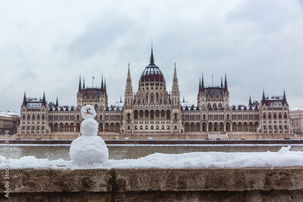 Hungarian parliament building at winter with snow. Snowman on the river bank, Budapest