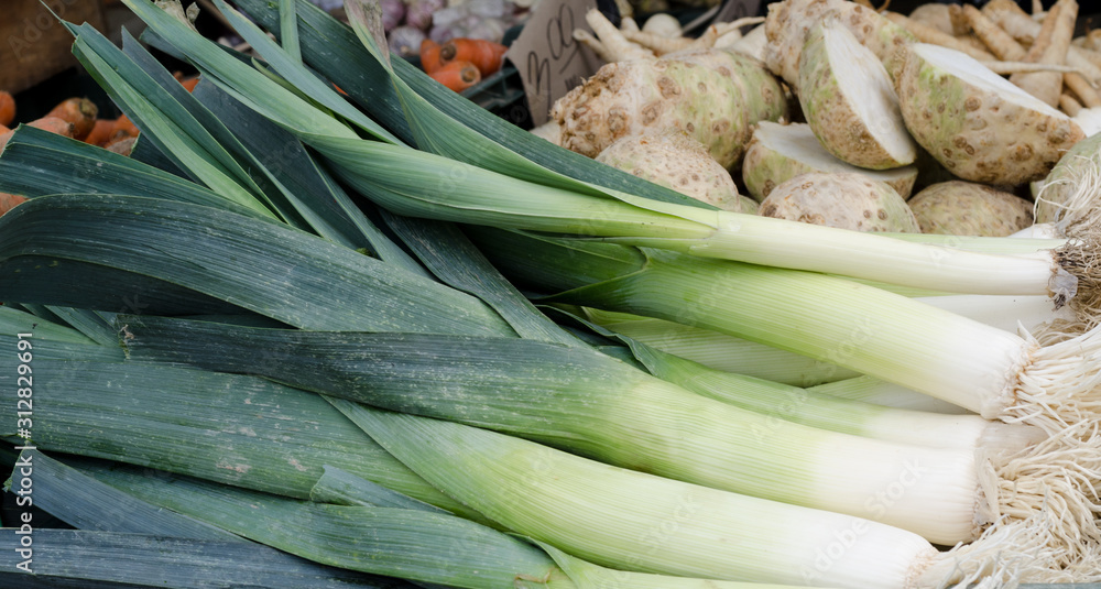 Fototapeta premium Stack of fresh leeks on a flea market counter. Fresh vegetables background.