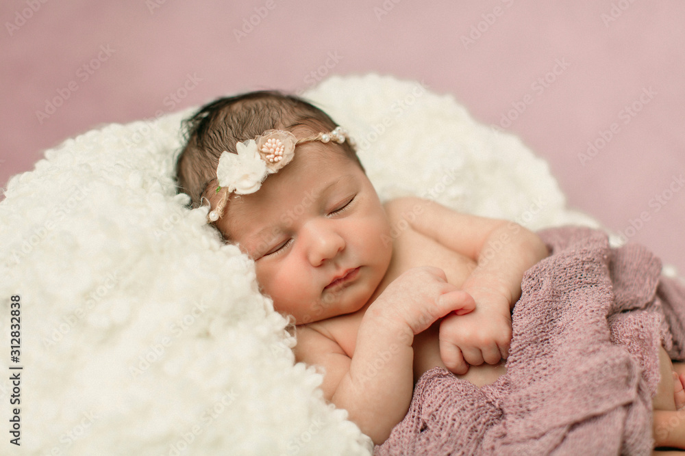 Sleeping newborn baby girl laying on a cream colored blanket on a pink purple backdrop with a headband in her hair Sleeping newborn baby girl laying on a cream colored blanket on a pink purple backdrop with a headband in her hair
