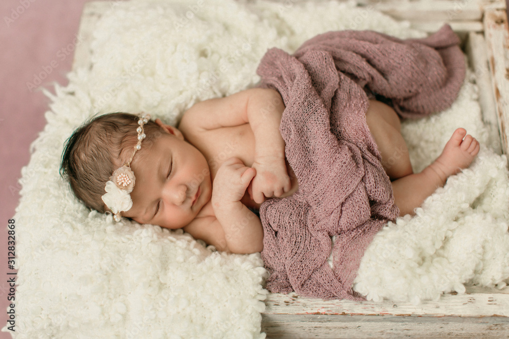 Sleeping newborn baby girl laying on a cream colored blanket on a pink purple backdrop with a headband in her hair Sleeping newborn baby girl laying on a cream colored blanket on a pink purple backdrop with a headband in her hair