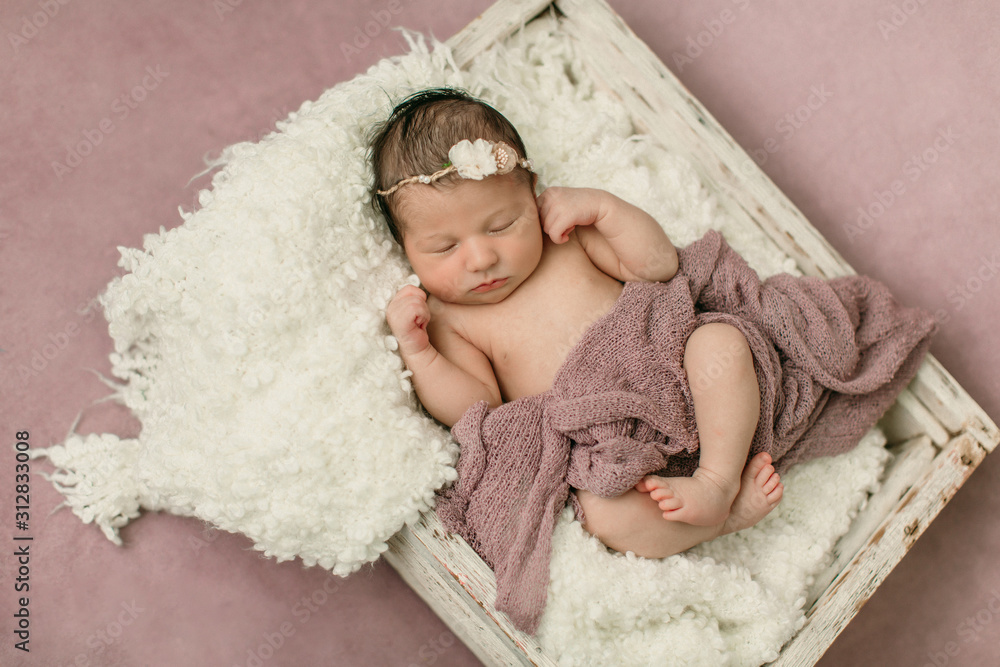 Sleeping newborn baby girl laying on a cream colored blanket on a pink purple backdrop with a headband in her hair Sleeping newborn baby girl laying on a cream colored blanket on a pink purple backdrop with a headband in her hair
