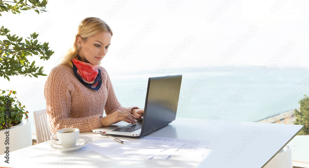 blonde woman with white skin is working outside at desk with laptop