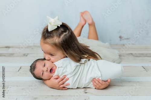 Foto 3 year old big sister kissing her newborn little sister in a cool tone white roo