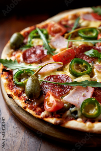 Pizza with ham, salami, jalapeno pepper, cherry tomatoes, capers, rocket and fresh basil. Close up.