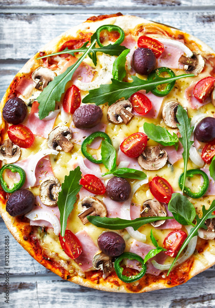 Pizza with cheese, cherry tomatoes, jalapeno pepper, kalamata olives, champignon mushrooms, fresh basil and rocket. Bright wooden background. Top view. Pizza with cheese, cherry tomatoes, jalapeno pepper, kalamata olives, champignon mushrooms, fresh basil and rocket. Bright wooden background. Top view.