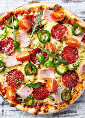 Pizza with ham, salami, jalapeno pepper, cherry tomatoes, cheese and rocket. Top view. 