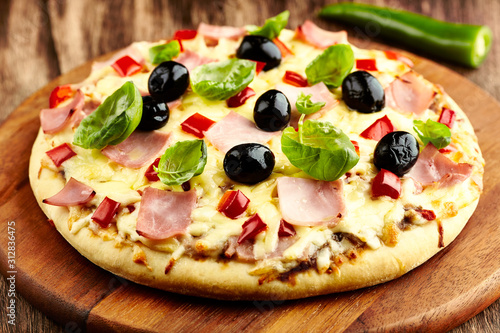 Pizza with ham, red pepper, black olives and fresh basil on rustic wooden background. 