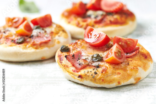 Mini pizzas with ham, cherry tomatoes, mozzarella and capers on bright wooden background. Close up. 