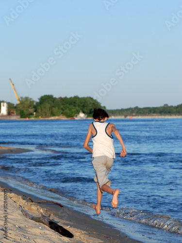 Barefoot cheerful boy running along the river bank on a sunny day