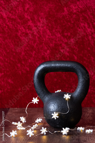 Holiday fitness, black kettlebell with white snowflake twinkle lights, against a red background