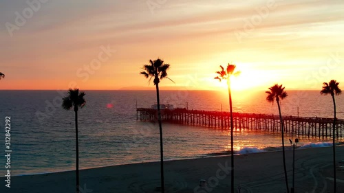 Cinematic aerial view of pier in Newport Beach, Orange County in California on sunny afternoon during golden hour sunset with palm trees in foreground. photo