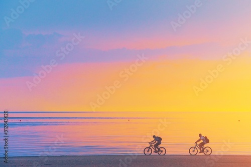 Biker silhouette riding along beach at sunset on bike Sporty company group of friends on bicycle outdoors Success achievement accomplishment and winning concept with cyclist mountain biking Copyspace