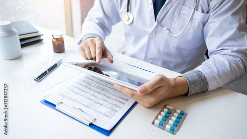 Doctor reading on a document report and writing on paperwork and searching treatment information at office, Medical healthcare concept.