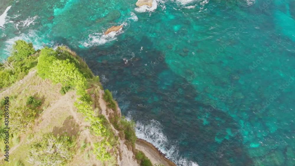 Drone tilt down over Atuh steep cliff on clear emerald ocean with hitting waves Drone tilt down over Atuh steep cliff on clear emerald ocean with hitting waves