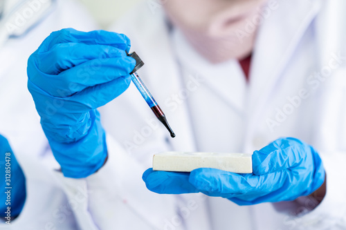 Scientist dropping a dark blue color chemical sampling into sampling plate close up. Scientist working with chemical in laboratory.