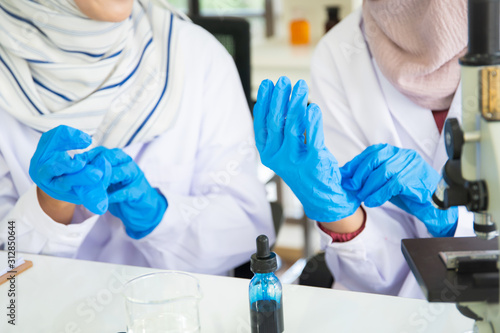 Two muslim woman scientist wearing a protection gloves before doing chemical experiment.