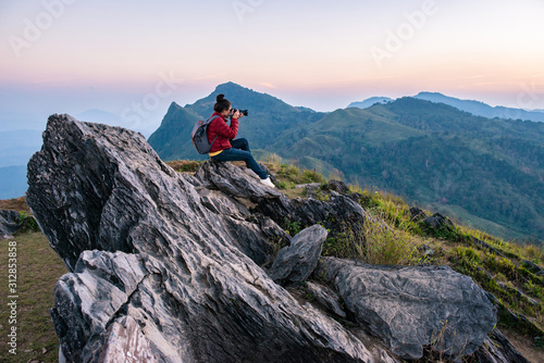 Tourist woman take a photographs of beautiful landscape of Doi Pha Tang in Chiang Rai province of Thailand at sunset. Doi Pha Tang is a mountain cliff over Thai-Laotian border.