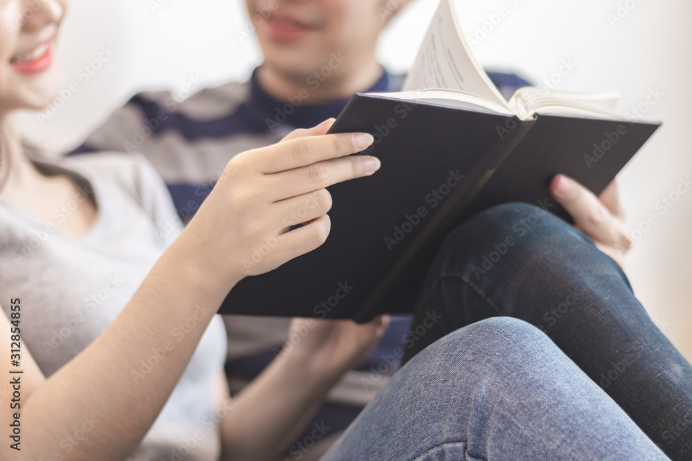 Fototapeta premium Lovely attractive young Asian couple man and woman with happy smile and reading book in romantic moment. Warm heart marriage and lover bonding and relationship. Husband and wife in love photo concept