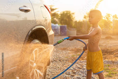 Happy asian little boy playing water from hose and spray to washing the car at outdoor in morning time