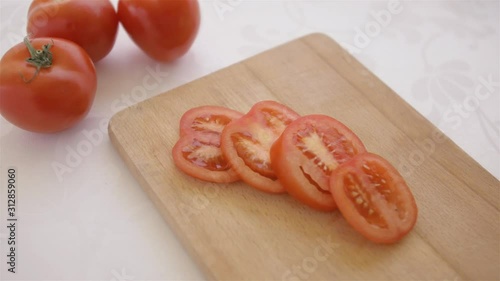 red tomatoes served on a wooden chopping board on white table background being put by male hand